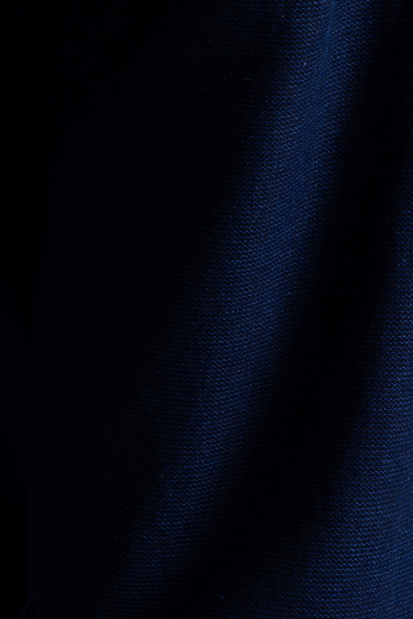 A close-up of dark navy blue textured fabric with a fine woven pattern and soft vertical folds.