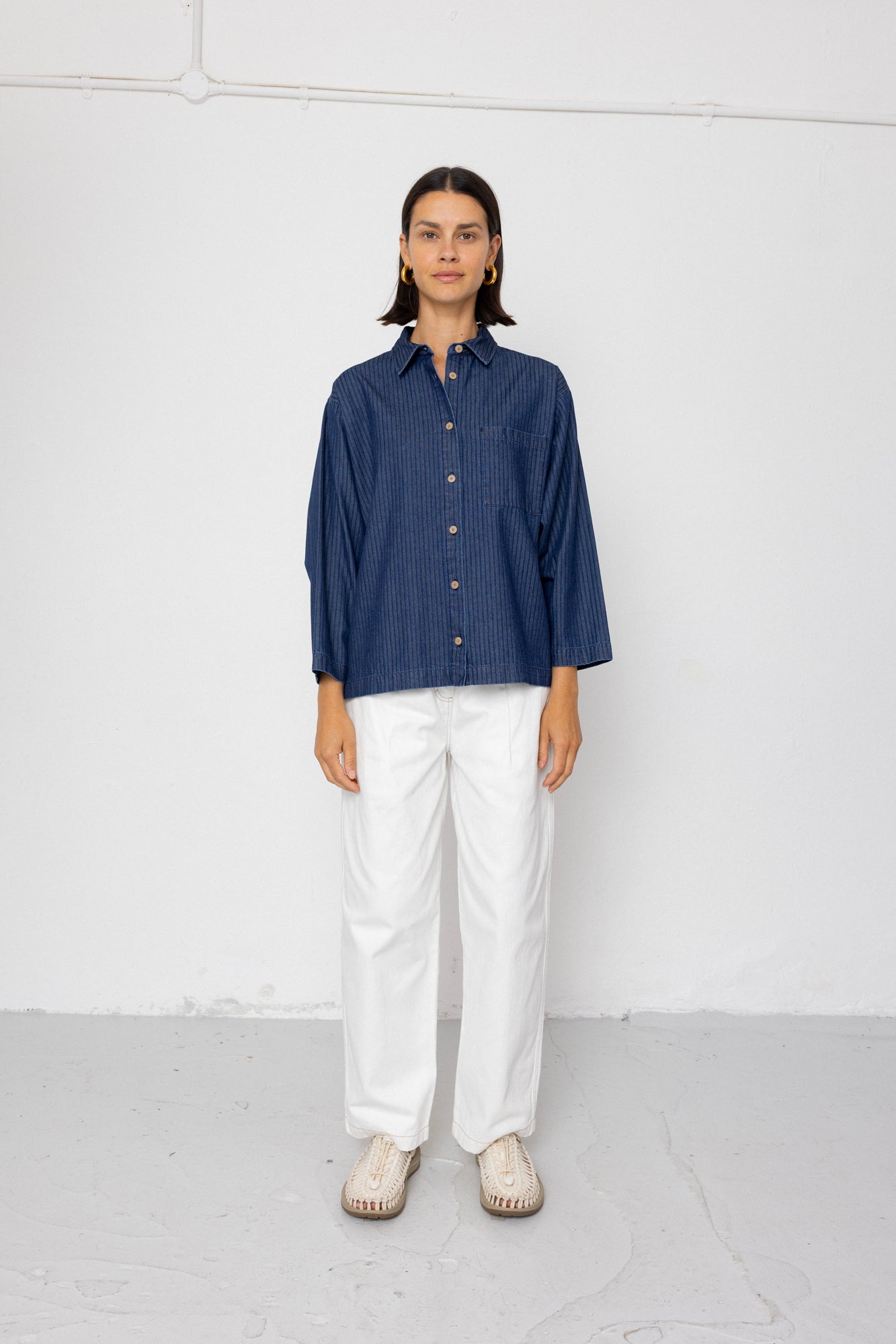 Person wearing a blue shirt and white pants against a white background