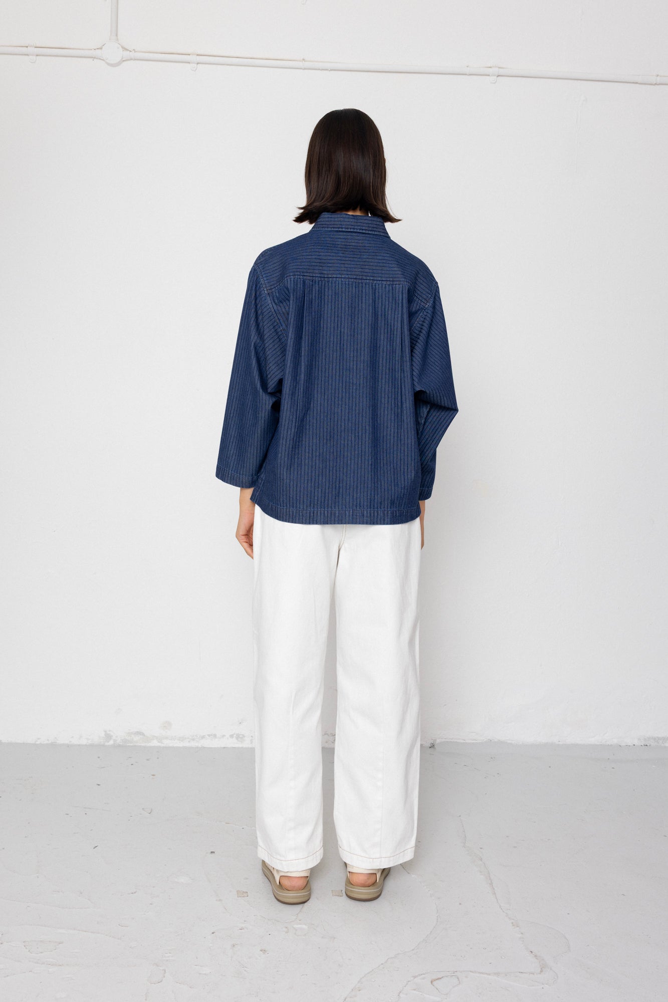 Person wearing a blue striped shirt and white pants against a white background