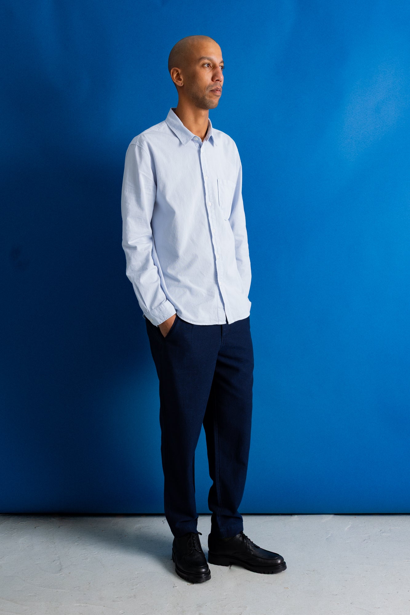 Model wearing bright navy trousers, pale blue shirt and black shoes against a bright blue background