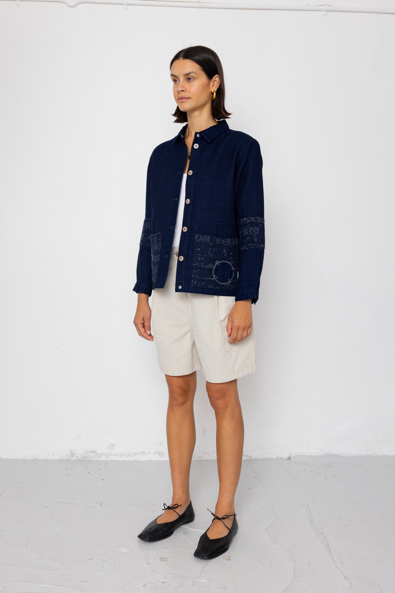 Woman wearing a navy jacket and white shorts against a white background