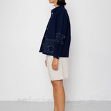 Woman wearing a navy blue textured jacket and white shorts on a white background