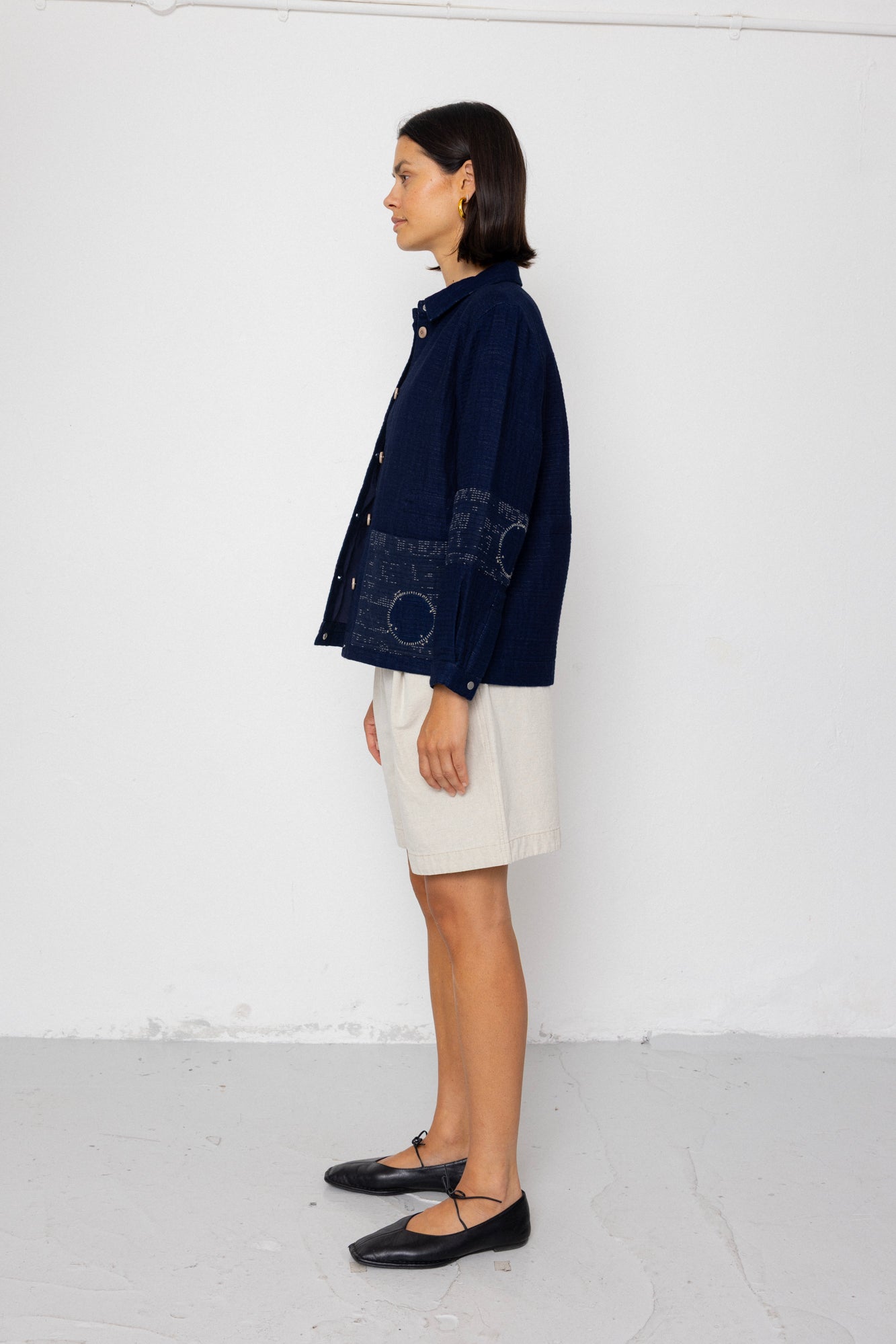 Woman wearing a navy blue textured jacket and white shorts on a white background