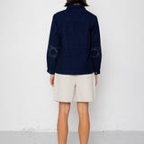 Person wearing a navy blue jacket and beige shorts against a white background