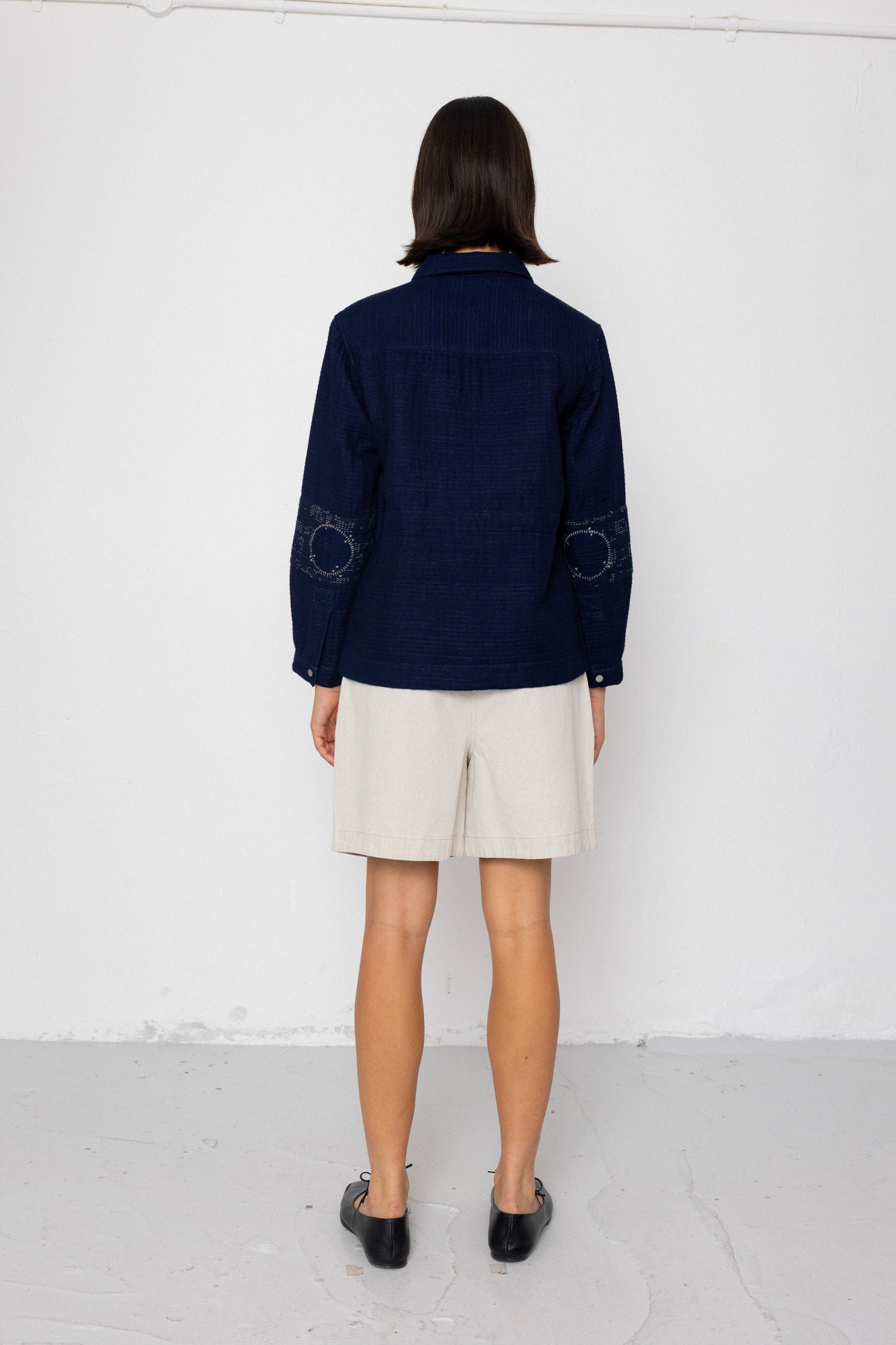 Person wearing a navy blue jacket and beige shorts against a white background