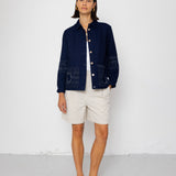 Woman wearing a navy blue textured jacket and white shorts on a white background