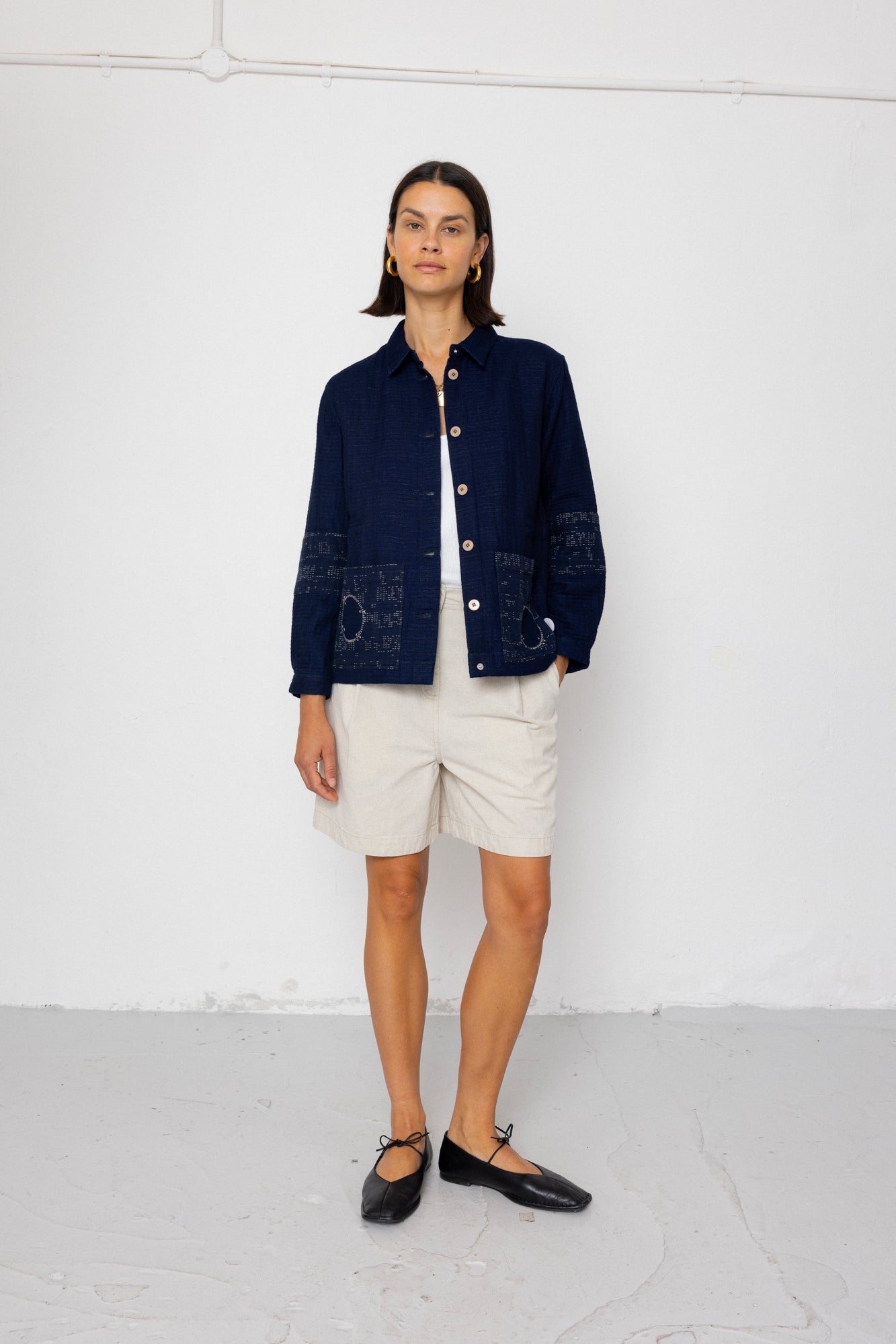 Woman wearing a navy blue textured jacket and white shorts on a white background