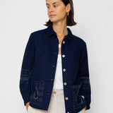Woman wearing a navy blue textured jacket and white pants on a white background