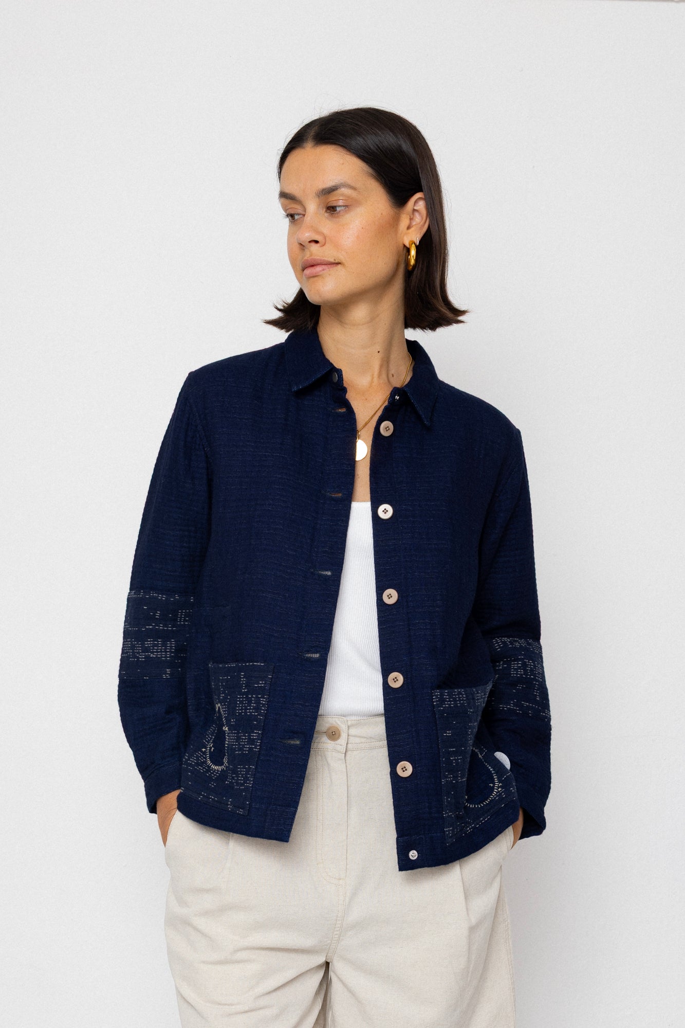 Woman wearing a navy blue textured jacket and white pants on a white background