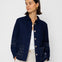 Woman wearing a navy blue textured jacket and white pants on a white background