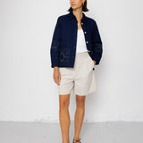 Woman wearing a navy jacket, white shirt, and shorts against a white background