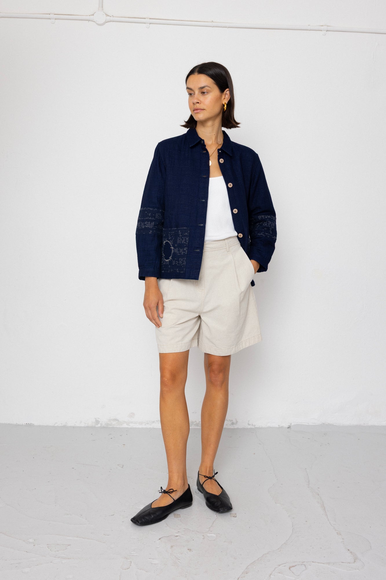 Woman wearing a navy jacket, white shirt, and shorts against a white background