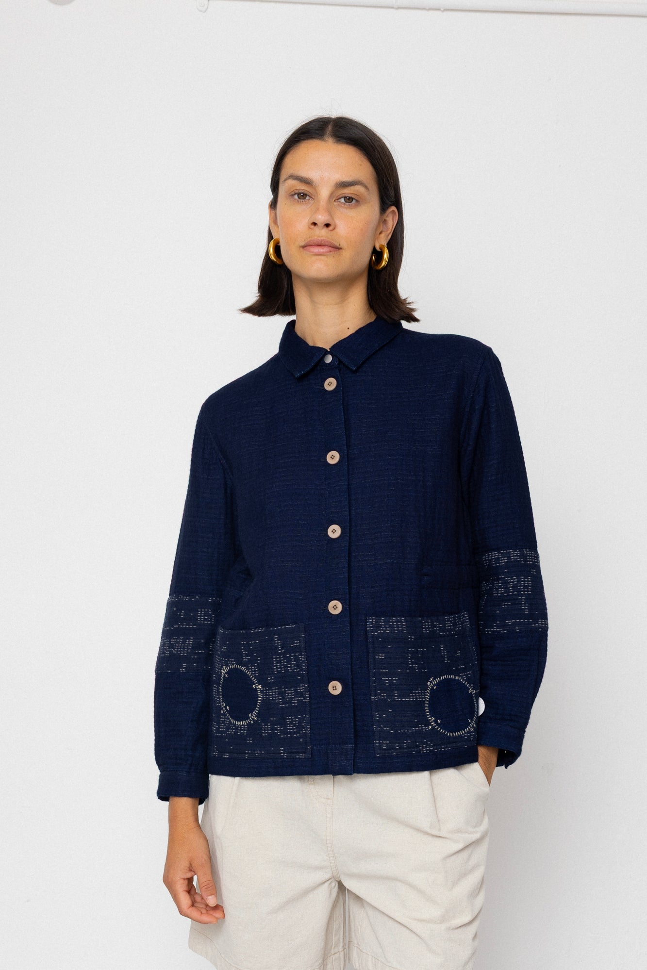 Person wearing a dark blue jacket with patterned patches on a white background