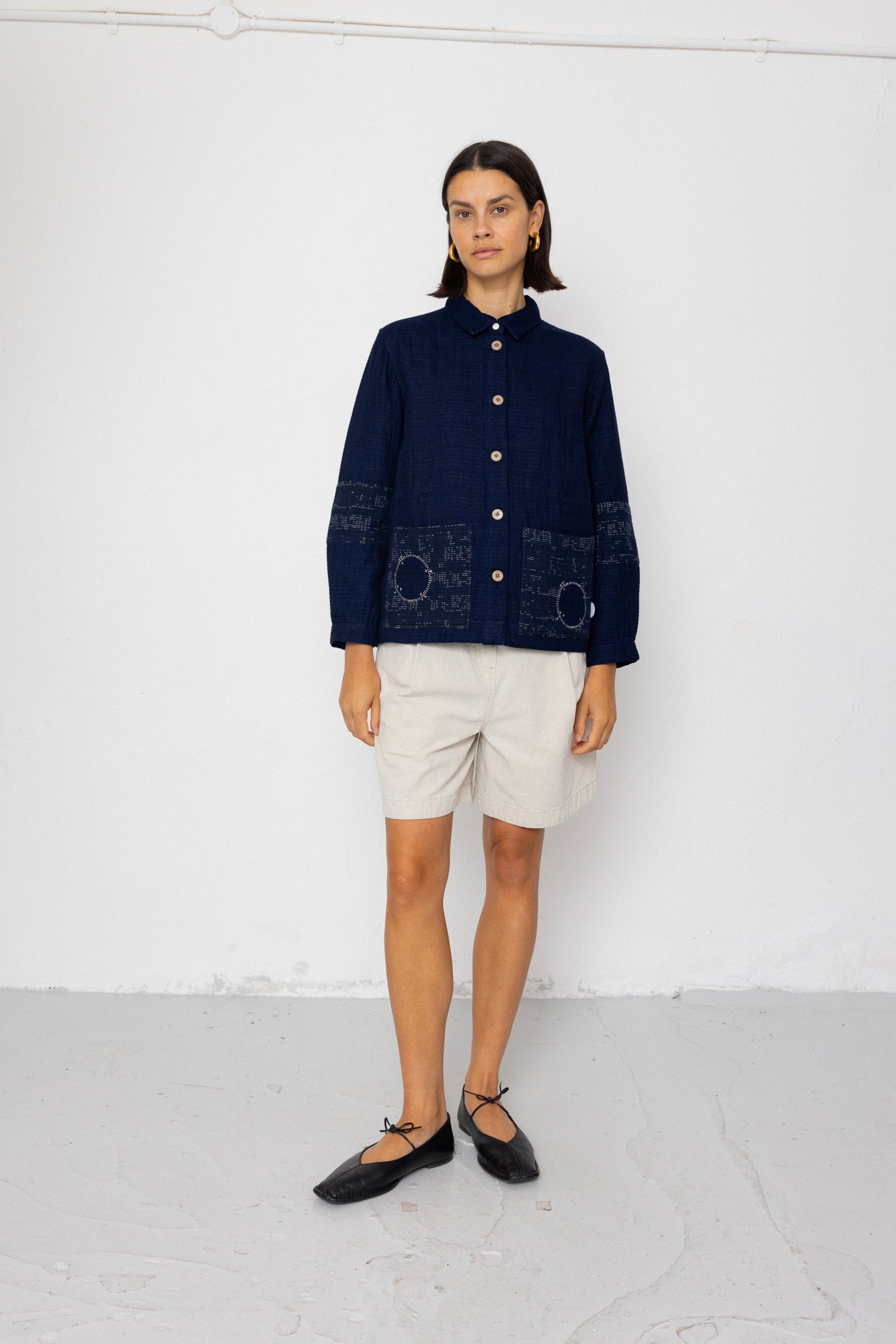 Person wearing a dark blue jacket with white shorts against a white background