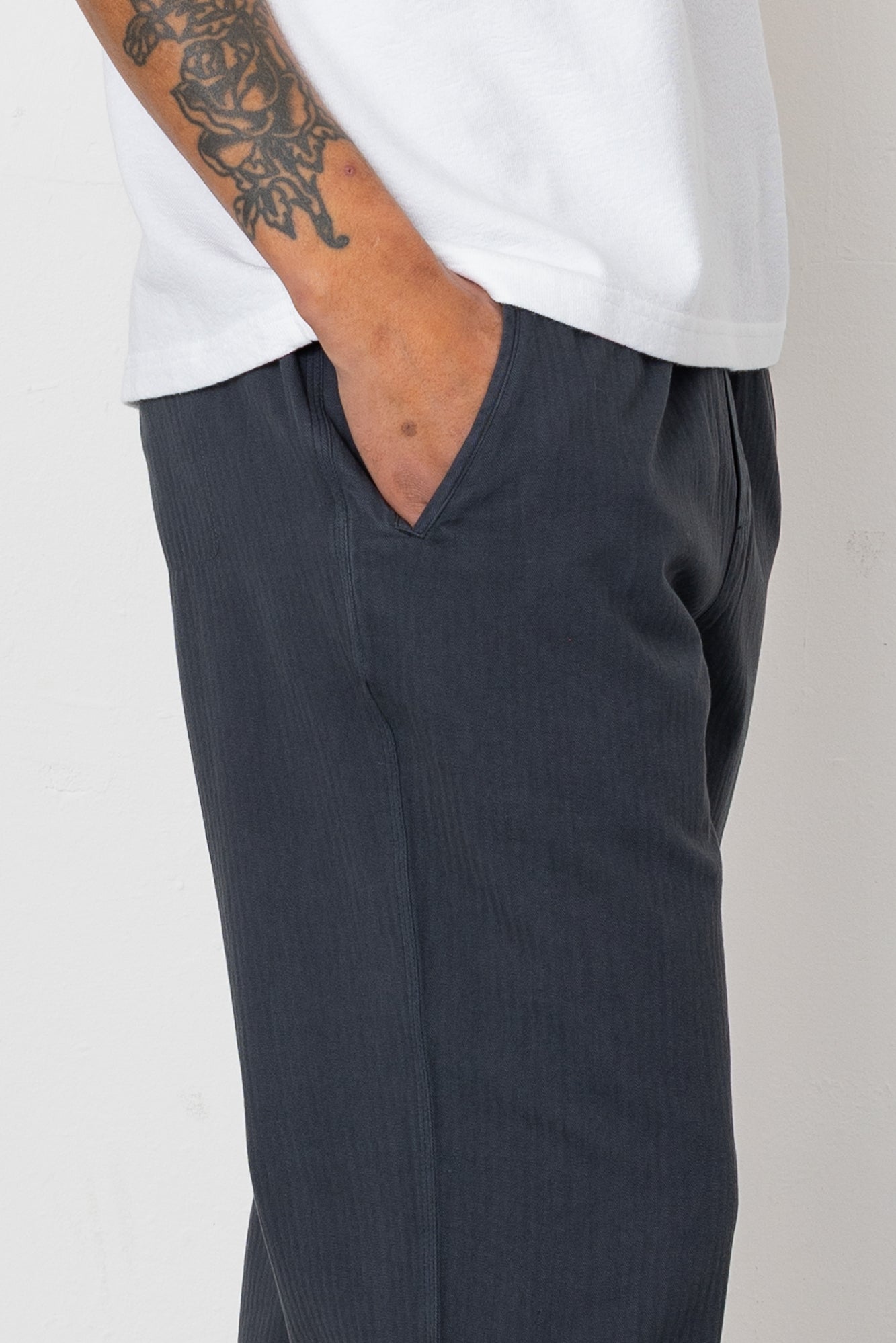 Person wearing dark gray pants and a white shirt on a plain background