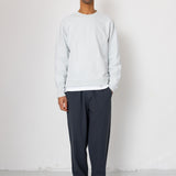 Man wearing a light gray sweatshirt and dark pants standing against a white background