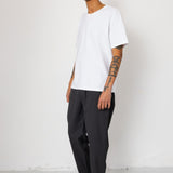 Man wearing a white t-shirt, black pants, and gray sneakers against a white background