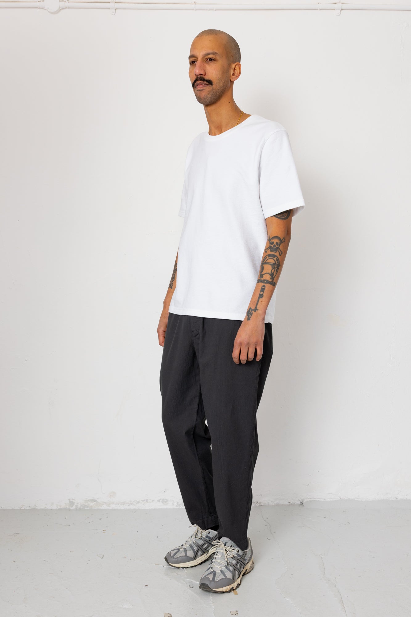 Man wearing a white t-shirt, black pants, and gray sneakers against a white background