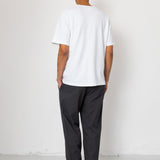 Person wearing a white t-shirt and dark pants standing against a white background