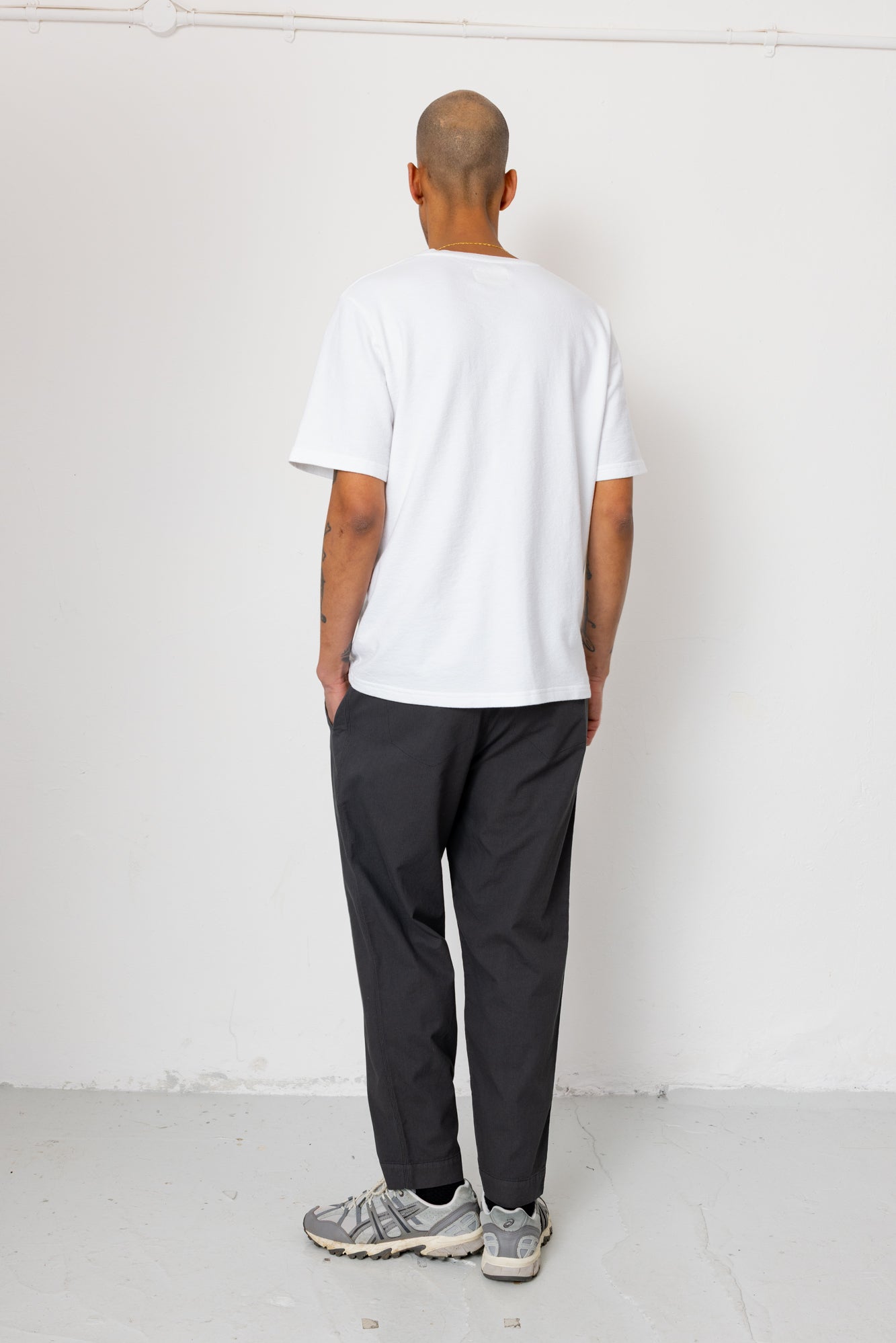 Person wearing a white t-shirt and dark pants standing against a white background