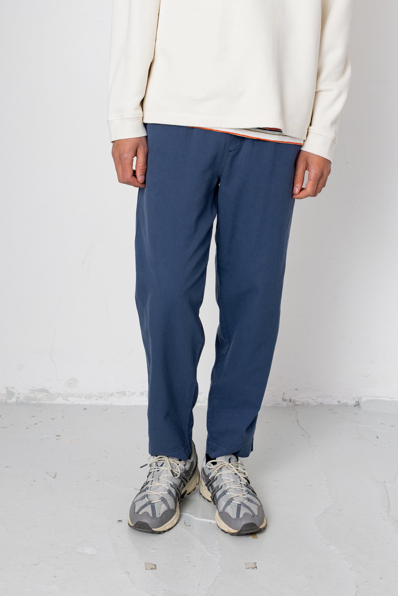 Person wearing blue pants and a cream sweater on a white background