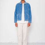 Man wearing a blue jacket, white shirt, and beige pants against a white background