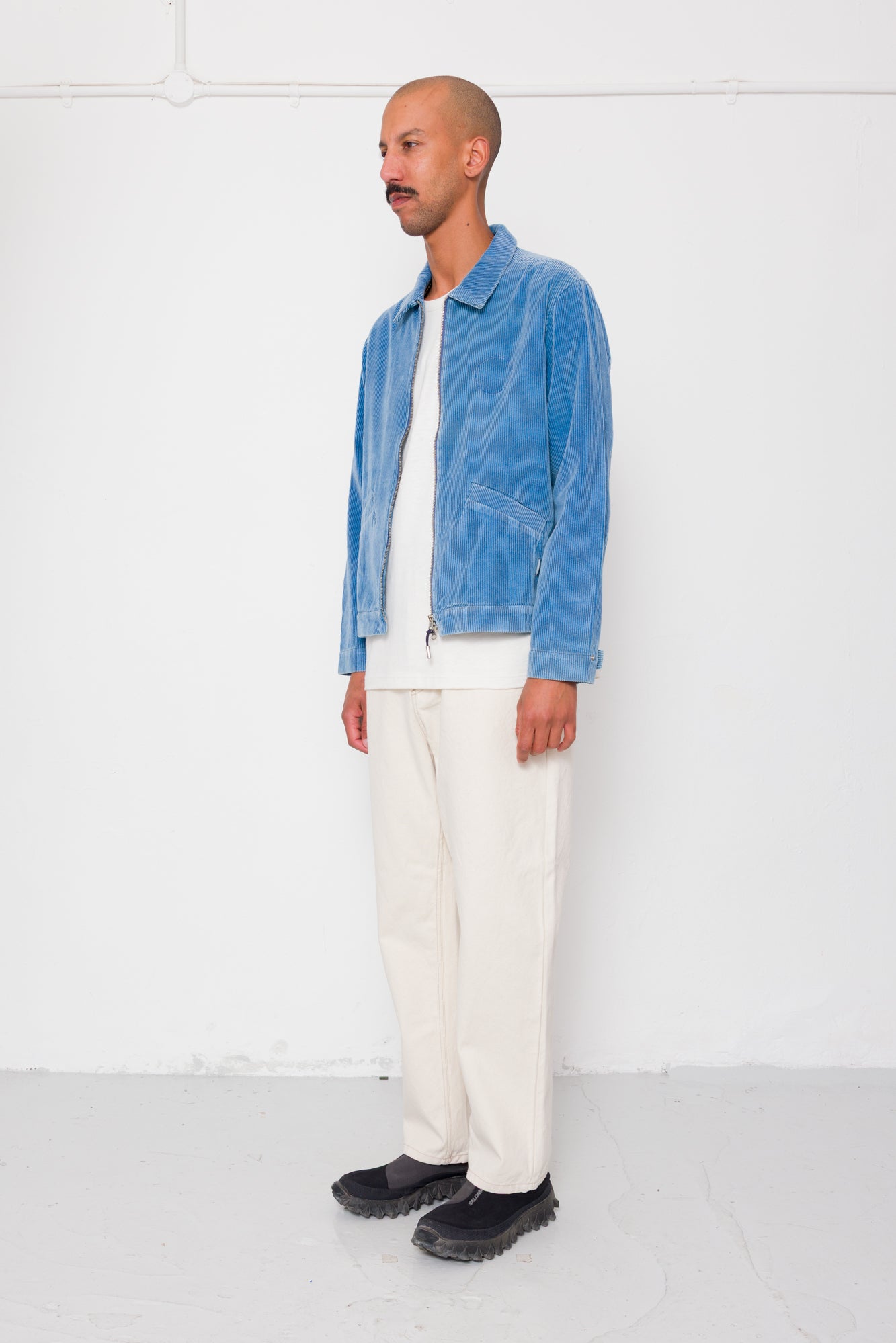 Man wearing a blue jacket, white shirt, and white pants against a white background