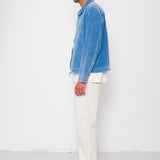 Man wearing a blue shirt and white pants standing against a white background