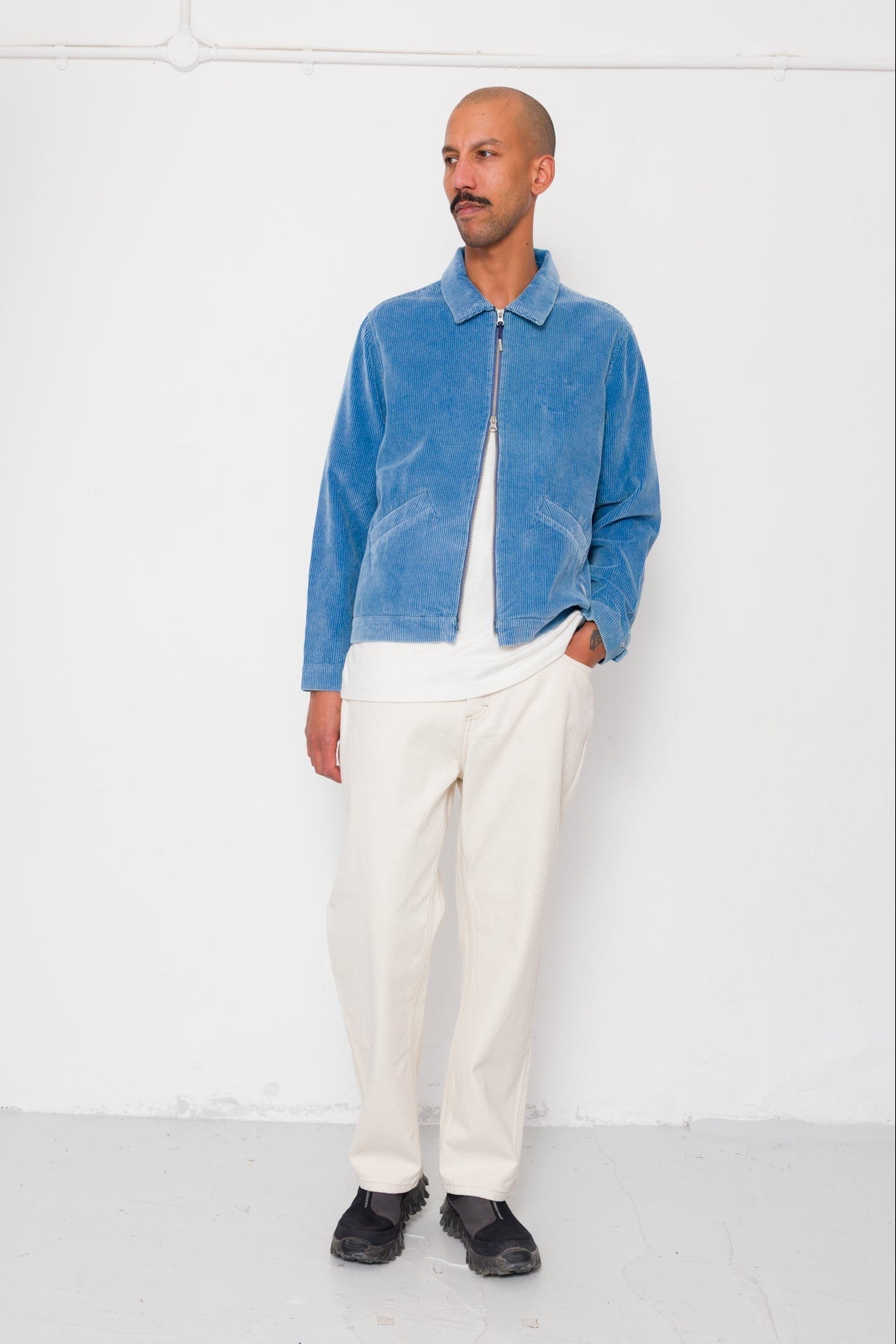 Man wearing a blue jacket and white pants against a white background
