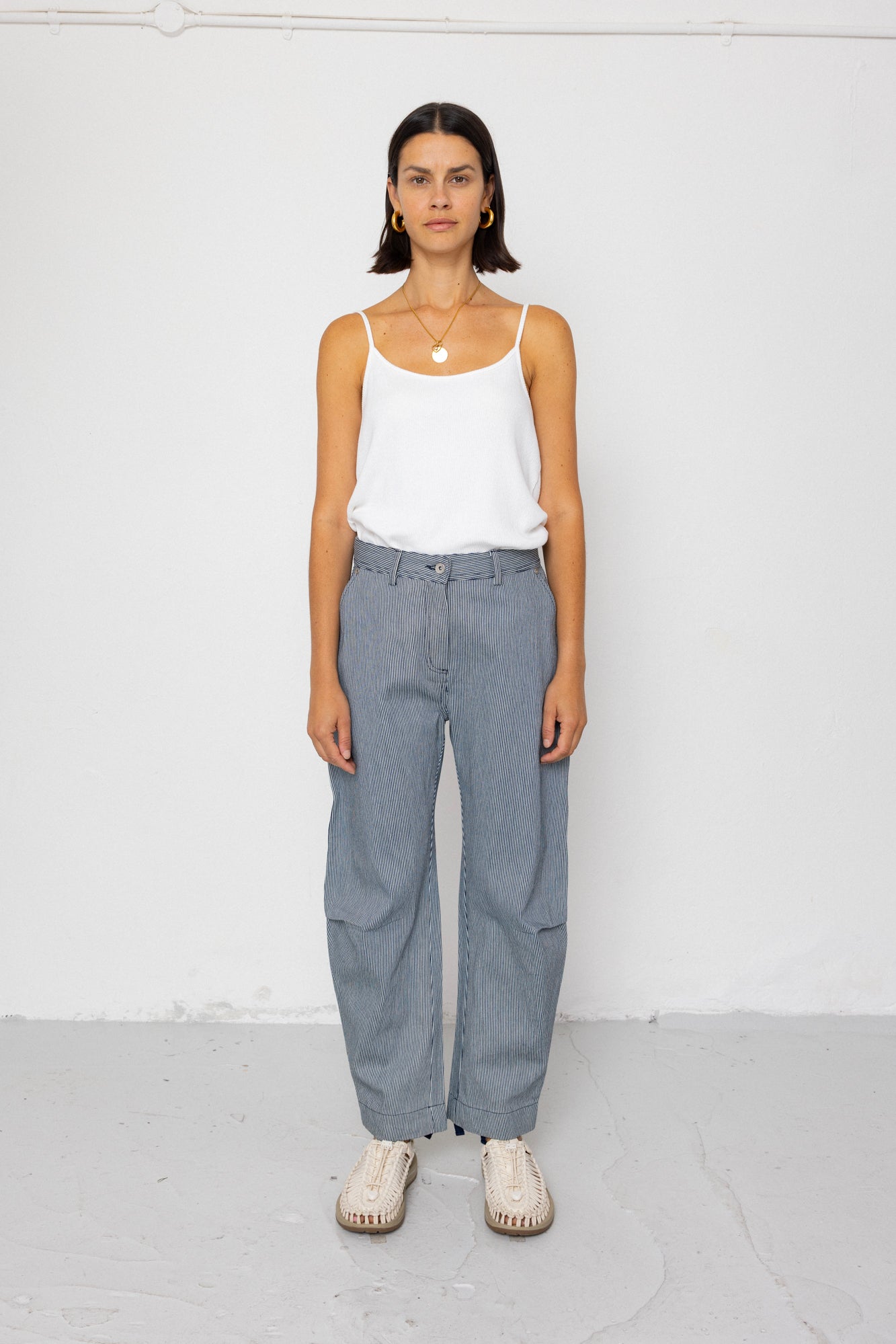 Person wearing a white tank top and striped denim trousers against a white background