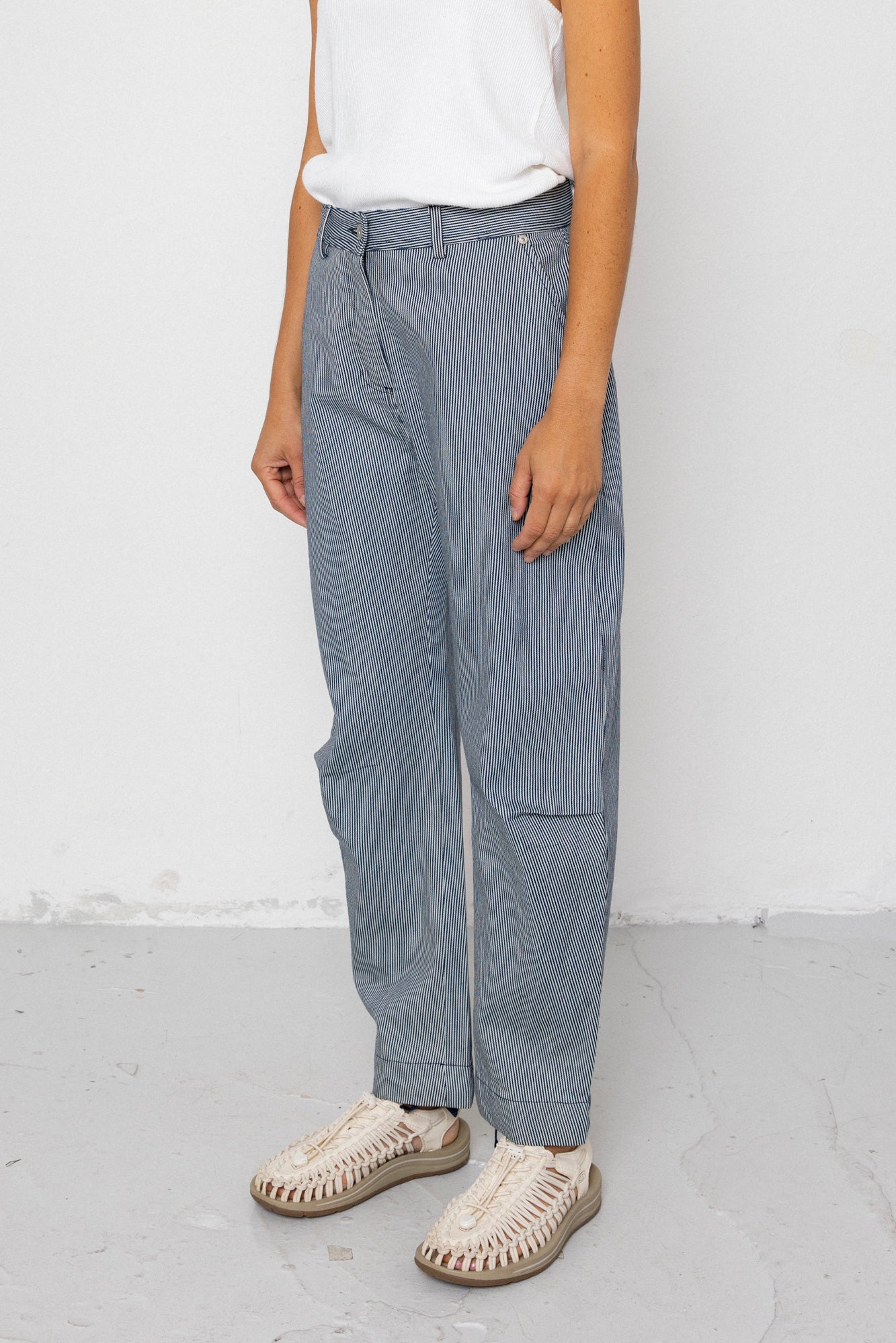 Person wearing denim striped pants and white shoes on a plain background