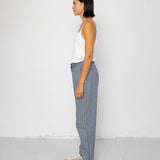 Person wearing a white top and striped denim pants standing against a white wall.