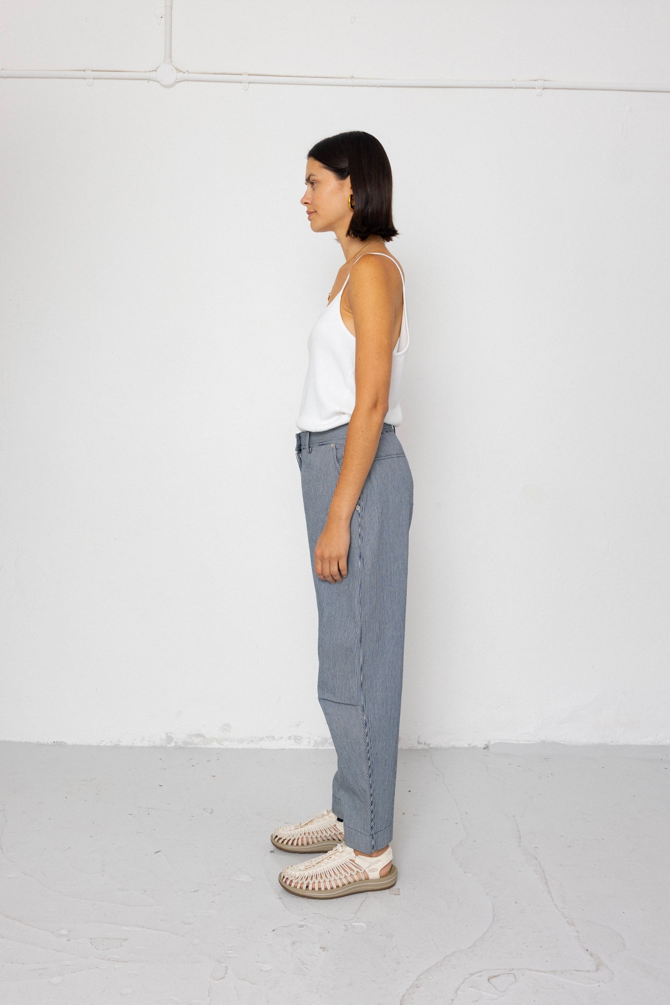 Person wearing a white top and striped denim pants standing against a white wall.