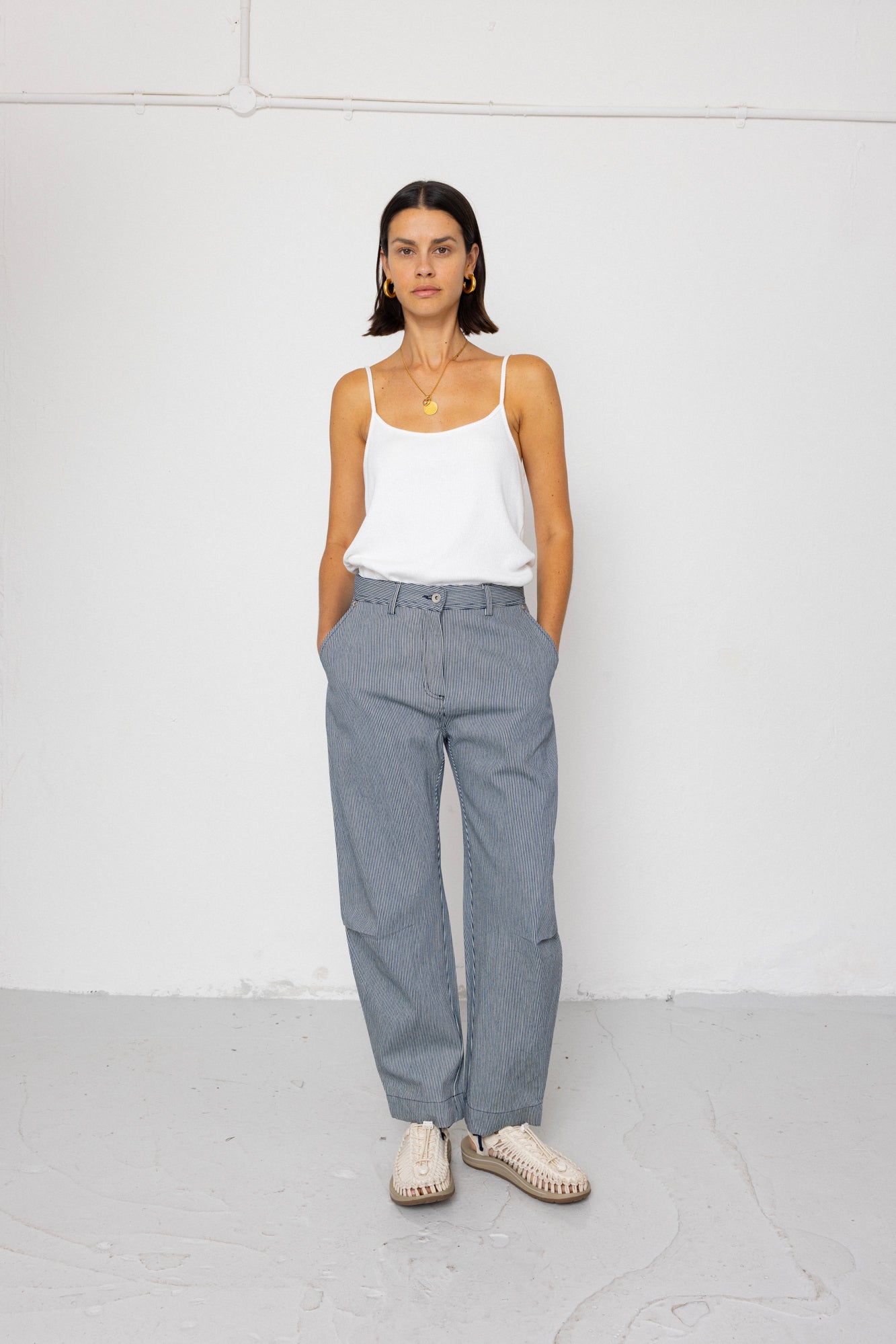Woman wearing a white tank top and striped denim pants against a white background