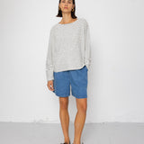 Person wearing a black and white striped long-sleeve top with blue shorts on a white background