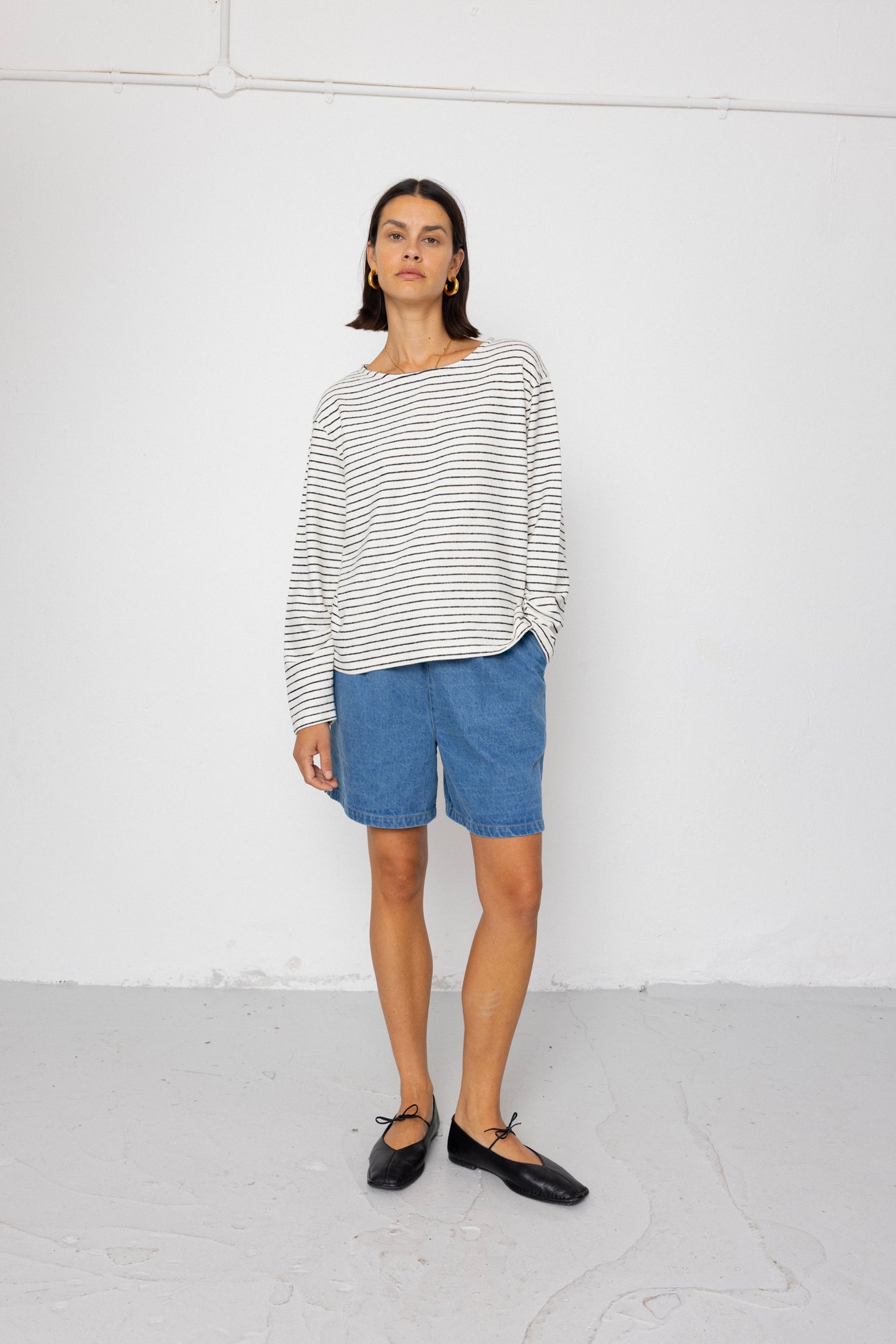 Person wearing a black and white striped long-sleeve top with blue shorts on a white background
