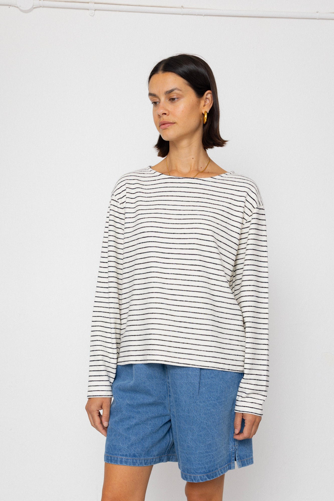 Person wearing a black and white striped long-sleeve top with blue shorts on a white background