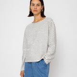 Person wearing a black and white striped long-sleeve top with blue shorts on a white background