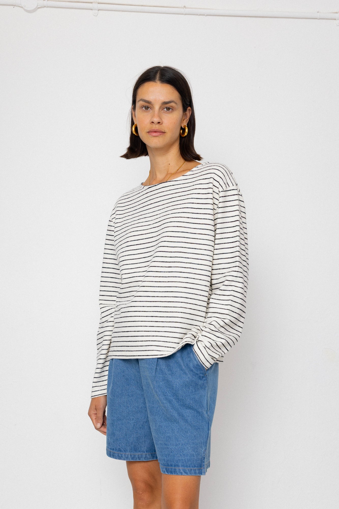 Person wearing a black and white striped long-sleeve top with blue shorts on a white background