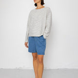 Person wearing a black and white striped long-sleeve top with blue shorts on a white background