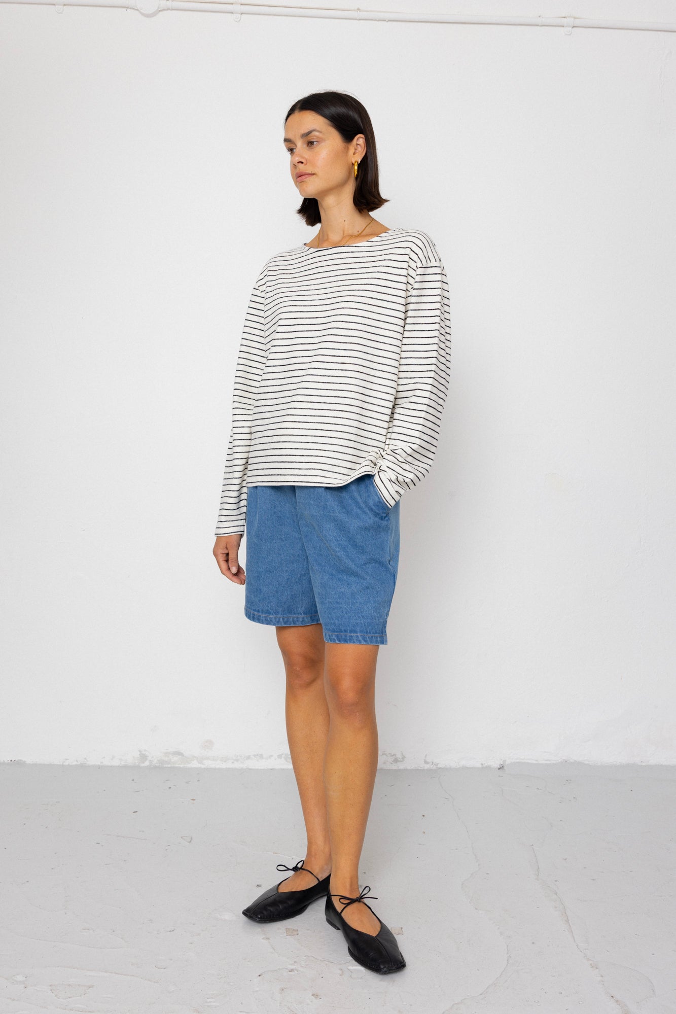 Person wearing a black and white striped long-sleeve top with blue shorts on a white background