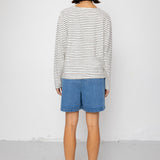 Person wearing a black and white striped long-sleeve top with blue shorts on a white background