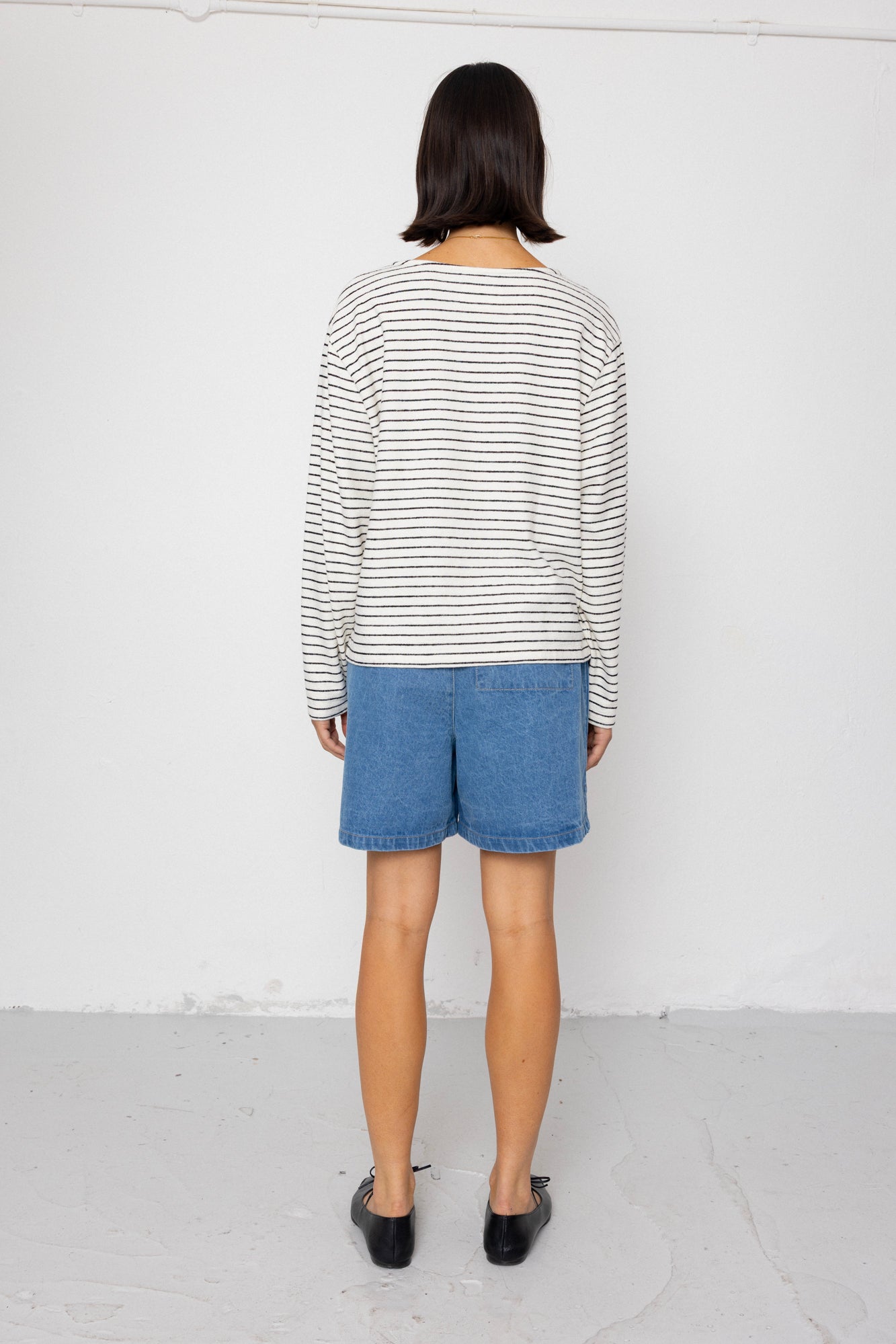 Person wearing a black and white striped long-sleeve top with blue shorts on a white background