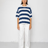 Person wearing a blue and white striped T-shirt with white pants on a plain background