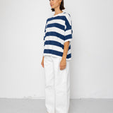 Person wearing a blue and white striped T-shirt with white pants on a plain background