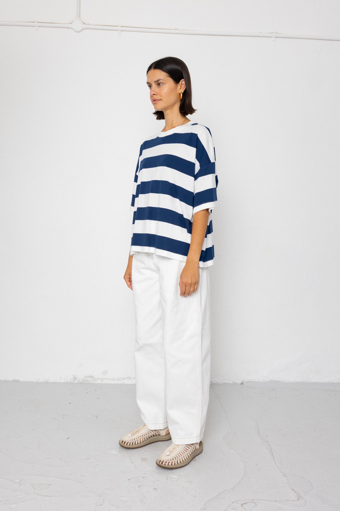 Person wearing a blue and white striped T-shirt with white pants on a plain background