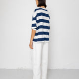 Person wearing a blue and white striped T-shirt with white pants on a plain background