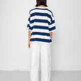 Person wearing a blue and white striped T-shirt with white pants on a plain background