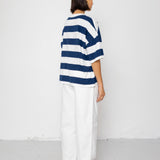 Person wearing a blue and white striped T-shirt with white pants on a plain background