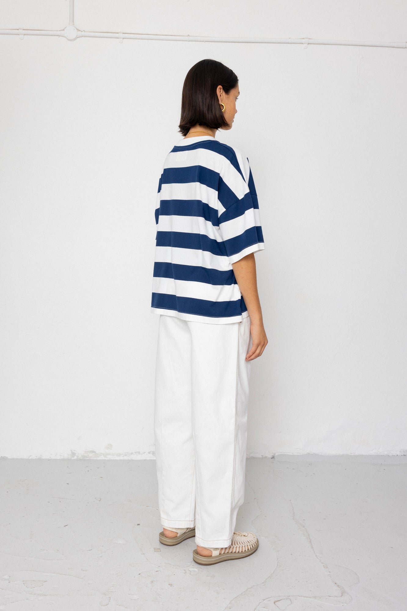 Person wearing a blue and white striped T-shirt with white pants on a plain background
